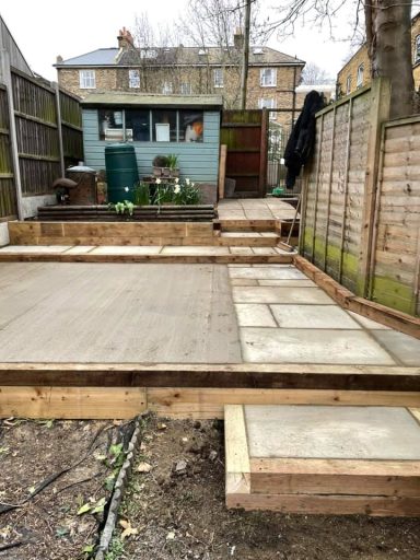 Stepped up sleepers surrounding a sandstone path, complemented by sleeper borders and a concrete base for a greenhouse