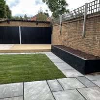 Contemporary garden featuring grey sandstone, a new lawn, wooden decking, and stylish sleeper borders