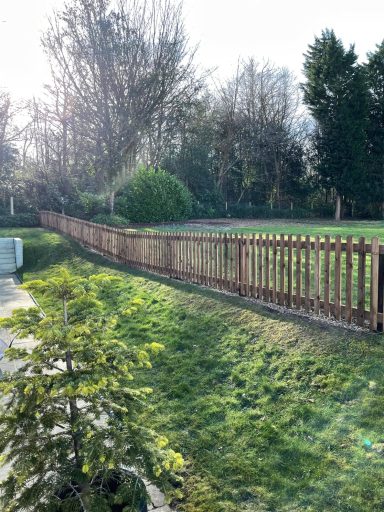 A wooden fence alongside a grassy area with trees in the background.