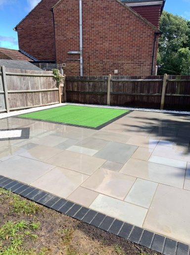Smooth Indian sandstone patio complemented by artificial grass and a pebble border for elegance